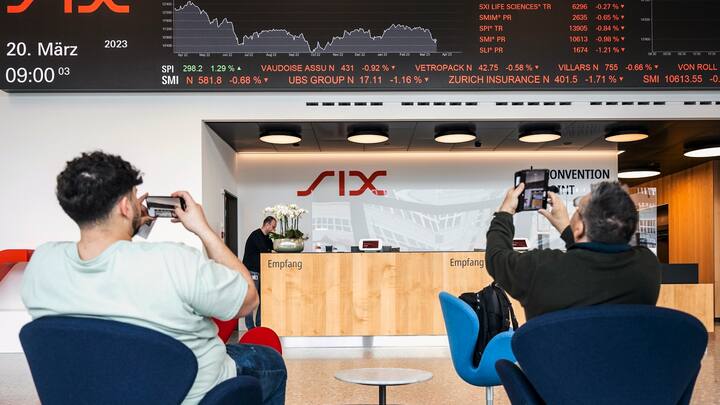 Des personnes prennent des photos d'un téléscripteur indiquant l'évolution des actions du groupe UBS, entre autres, à la SIX Swiss Exchange à Zurich, en Suisse, le 20 mars 2023. Les marchés financiers réagissent après le sauvetage de la banque en difficulté Credit Suisse par sa rivale suisse UBS, dans le cadre d'un accord soutenu par le gouvernement, pour un montant de trois milliards de dollars. UBS a perdu 13 % de sa valeur.