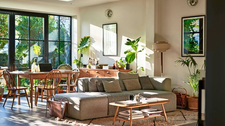 Salon confortable avec canapé et table basse, table à manger et chaises, avec portes-fenêtres donnant sur le jardin.