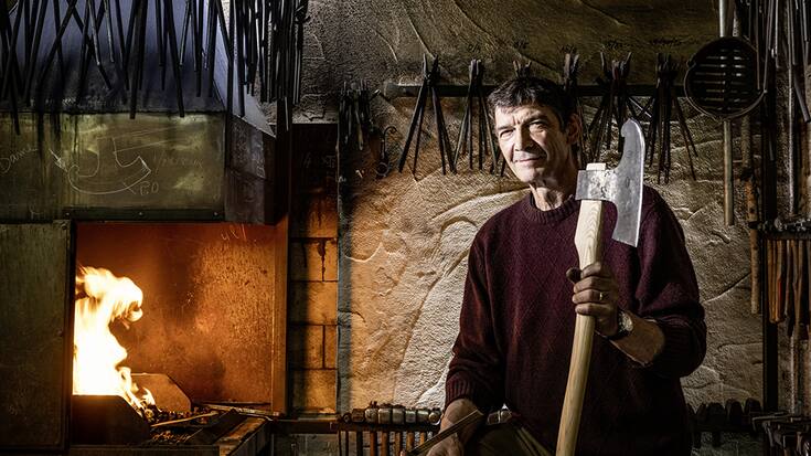 Serge Turberg dans sa forge de Malleray dans le Jura bernois. Il montre une hache de coeur semblable à celles qu'on utilisait au Moyen Age pour bâtir les églises.