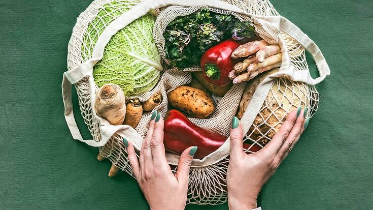 Les mains d'une femme tenant un sac d'épicerie en maille écologique avec divers légumes sur un fond sombre, vue de dessus. Concept de mode de vie sans plastique et sans déchets.
