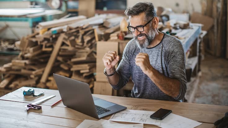 Carpenter owner working at office on laptop. He is happy about good news