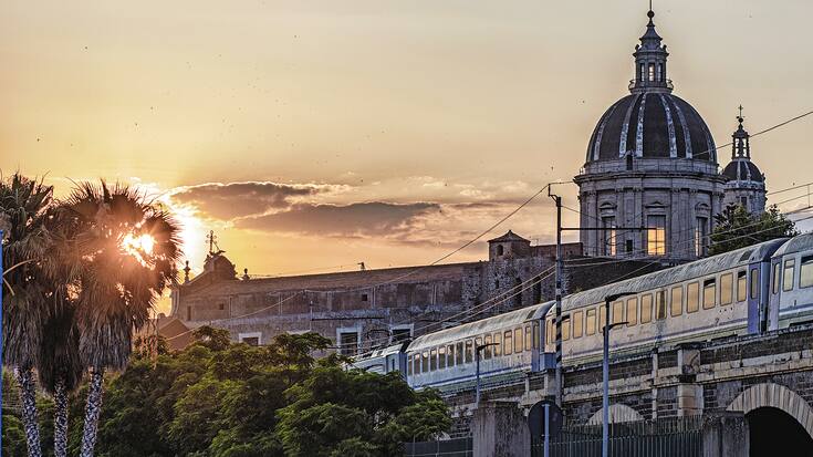 Catania, passing the train at sunset over the marina arches. View of the Dome and the city ancient walls