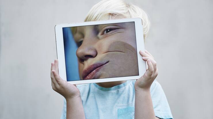 Young boy holding a digital tablet with an image of his face pressed against the screen.