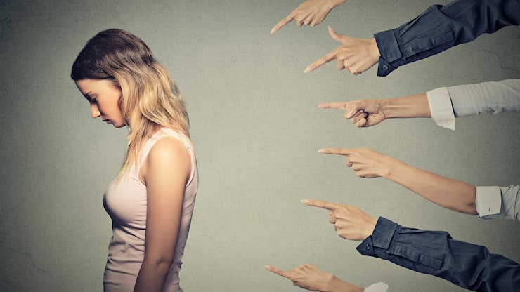 Concept of accusation guilty person girl. Side profile sad upset woman looking down many fingers pointing at her back isolated on grey office wall background. Human face expression emotion feeling