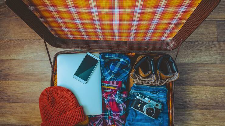 Open suitcase with casual clothes, laptop and phone