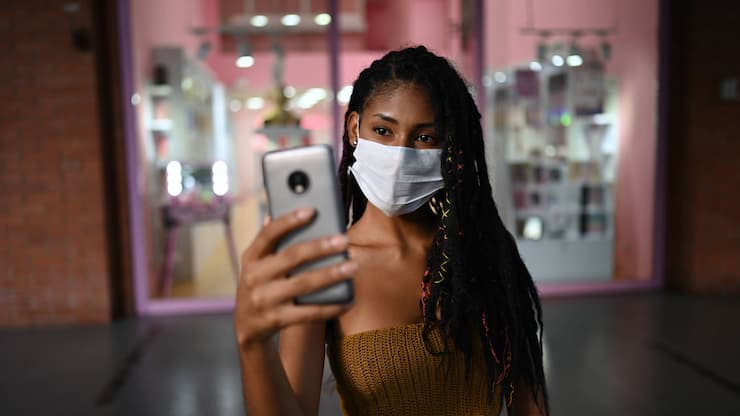 Creative Portrait of attractive young afro latin woman wearing a facemask and doing a videocall on smartphone in a commercial mall, Colombia, Model released Copyright: xNanoxCalvox