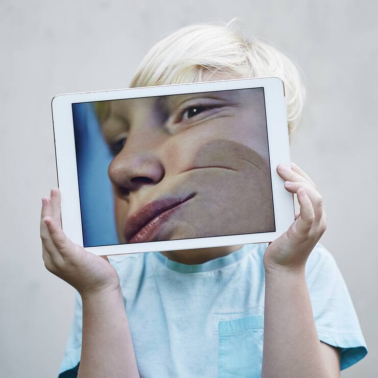 Young boy holding a digital tablet with an image of his face pressed against the screen.