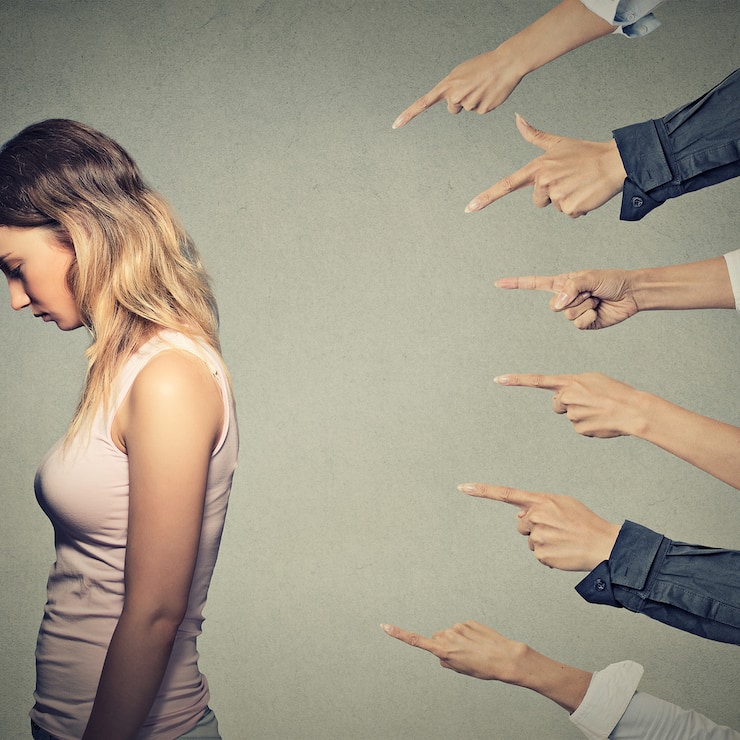 Concept of accusation guilty person girl. Side profile sad upset woman looking down many fingers pointing at her back isolated on grey office wall background. Human face expression emotion feeling