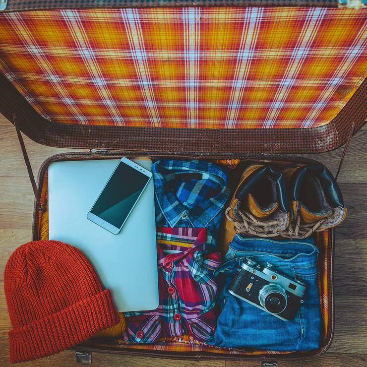 Open suitcase with casual clothes, laptop and phone