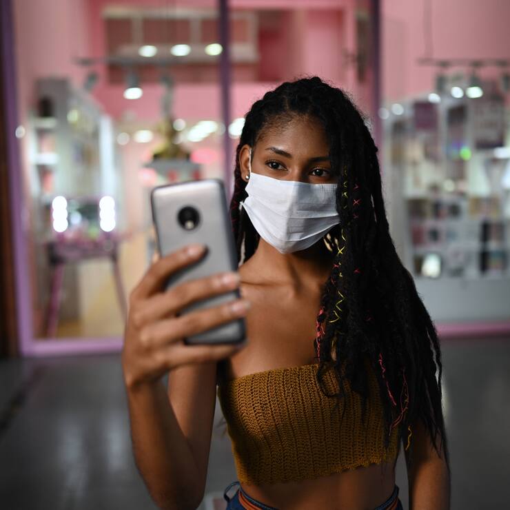 Creative Portrait of attractive young afro latin woman wearing a facemask and doing a videocall on smartphone in a commercial mall, Colombia, Model released Copyright: xNanoxCalvox