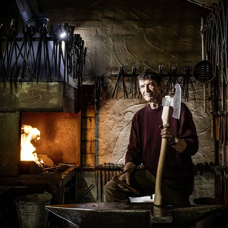 Serge Turberg dans sa forge de Malleray dans le Jura bernois. Il montre une hache de coeur semblable à celles qu'on utilisait au Moyen Age pour bâtir les églises.