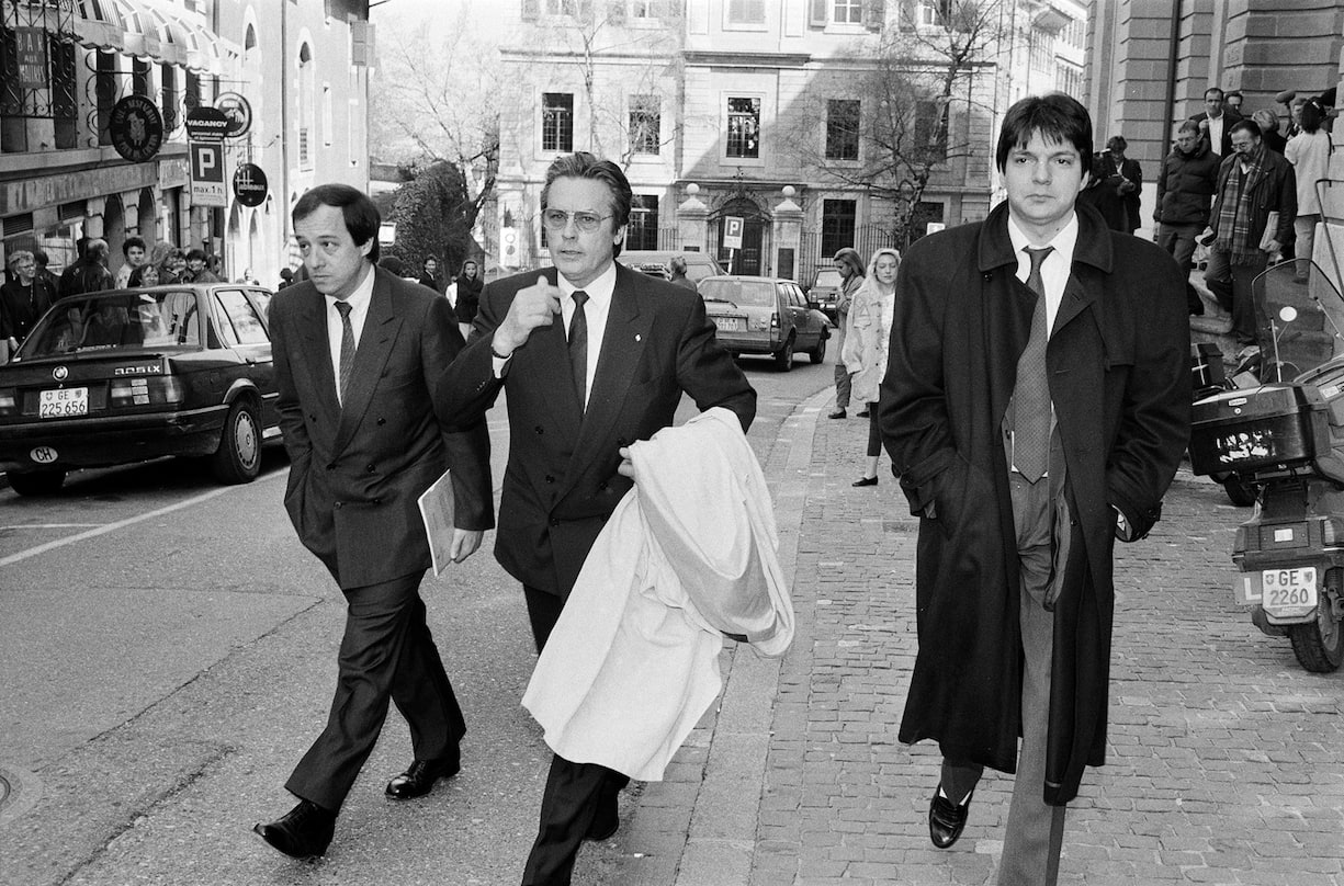 Actor Alain Delon leaves the court accompanied by his lawyers Charles Poncet, left, and Dominique Warluzel, right, after a hearing of the case Alain Delon Diffusion S.A., pictured in Geneva, Switzerland, on April 10, 1991. (KEYSTONE/Str)Der Schauspieler Alain Delon verlaesst nach der Gerichtsverhandlung in Sachen Alain Delon Diffusion S. A. das Gericht in Genf in Begleitung seiner Anwaelte Charles Poncet, links, und Dominique Warluzel, rechts. Aufgenommen am 10. April 1991. (KEYSTONE/Str)