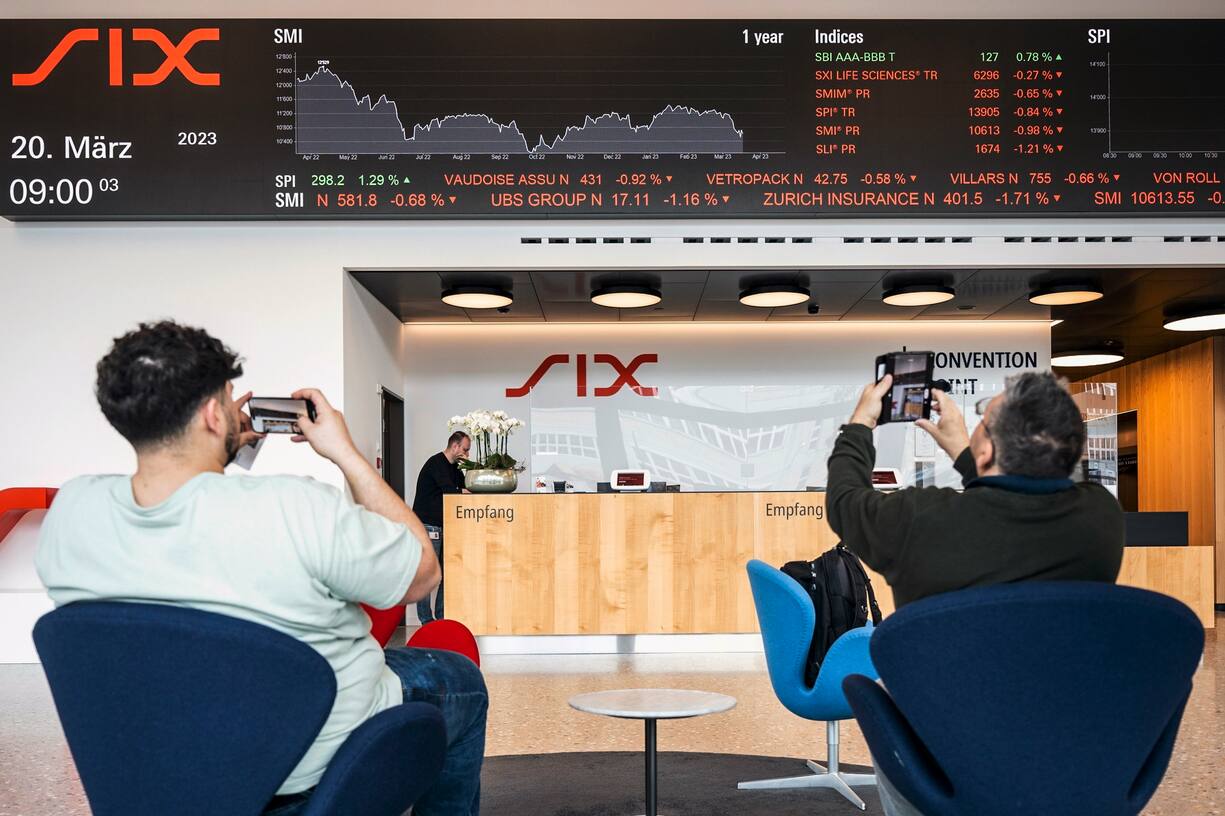 Des personnes prennent des photos d'un téléscripteur indiquant l'évolution des actions du groupe UBS, entre autres, à la SIX Swiss Exchange à Zurich, en Suisse, le 20 mars 2023. Les marchés financiers réagissent après le sauvetage de la banque en difficulté Credit Suisse par sa rivale suisse UBS, dans le cadre d'un accord soutenu par le gouvernement, pour un montant de trois milliards de dollars. UBS a perdu 13 % de sa valeur.