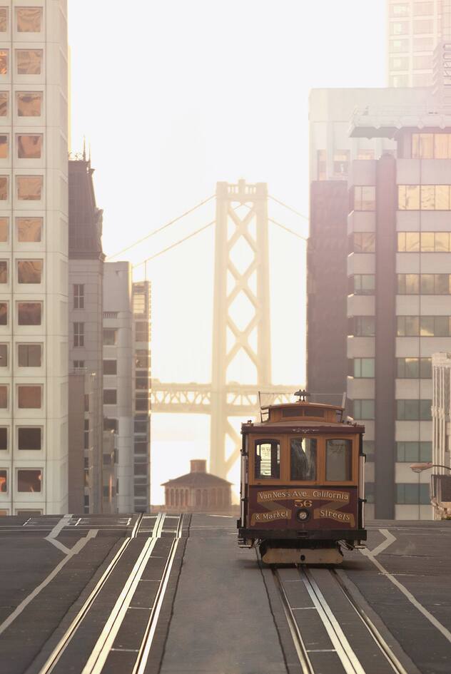 The Van Ness cable car as it reaches the top of Nob Hill in San Francisco on California Street with a view of the Bay Bridge in the background.