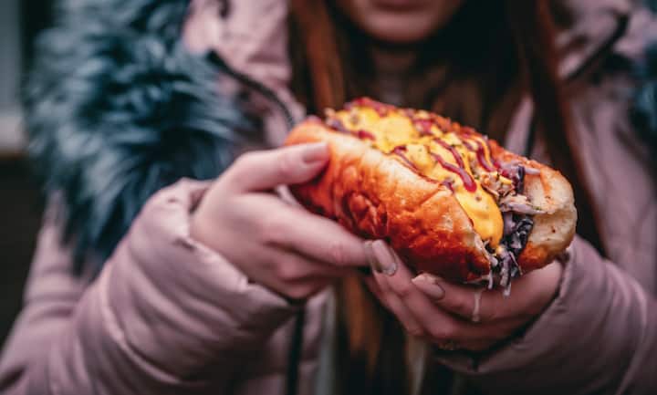 Philly cheese steak sandwich with meat, vegetables, cheese and sause in the hands of woman. Street food outdoor winter