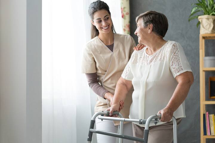 Smiling beautiful caregiver and disabled old lady with walker at home