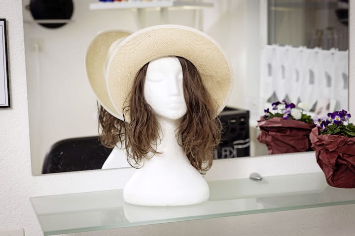 La «pascalette»,  une perruque confectionnée par Pascale Burri, permettant d’associer les cheveux coupés, collés sur un fin bandeau, à un accessoire type foulard ou, comme ici, à un chapeau.