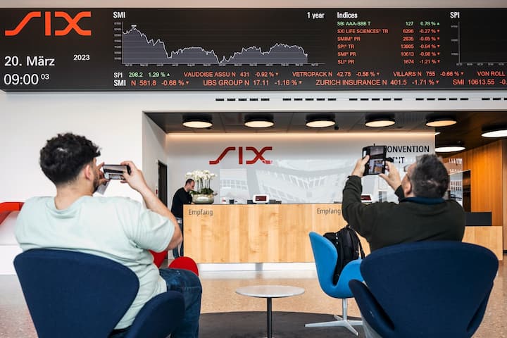 Des personnes prennent des photos d'un téléscripteur indiquant l'évolution des actions du groupe UBS, entre autres, à la SIX Swiss Exchange à Zurich, en Suisse, le 20 mars 2023. Les marchés financiers réagissent après le sauvetage de la banque en difficulté Credit Suisse par sa rivale suisse UBS, dans le cadre d'un accord soutenu par le gouvernement, pour un montant de trois milliards de dollars. UBS a perdu 13 % de sa valeur.